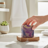 Blanche Bete inspired Soap Bar in Purple Swirls with a Hand Reaching for It on a Wooden Dish