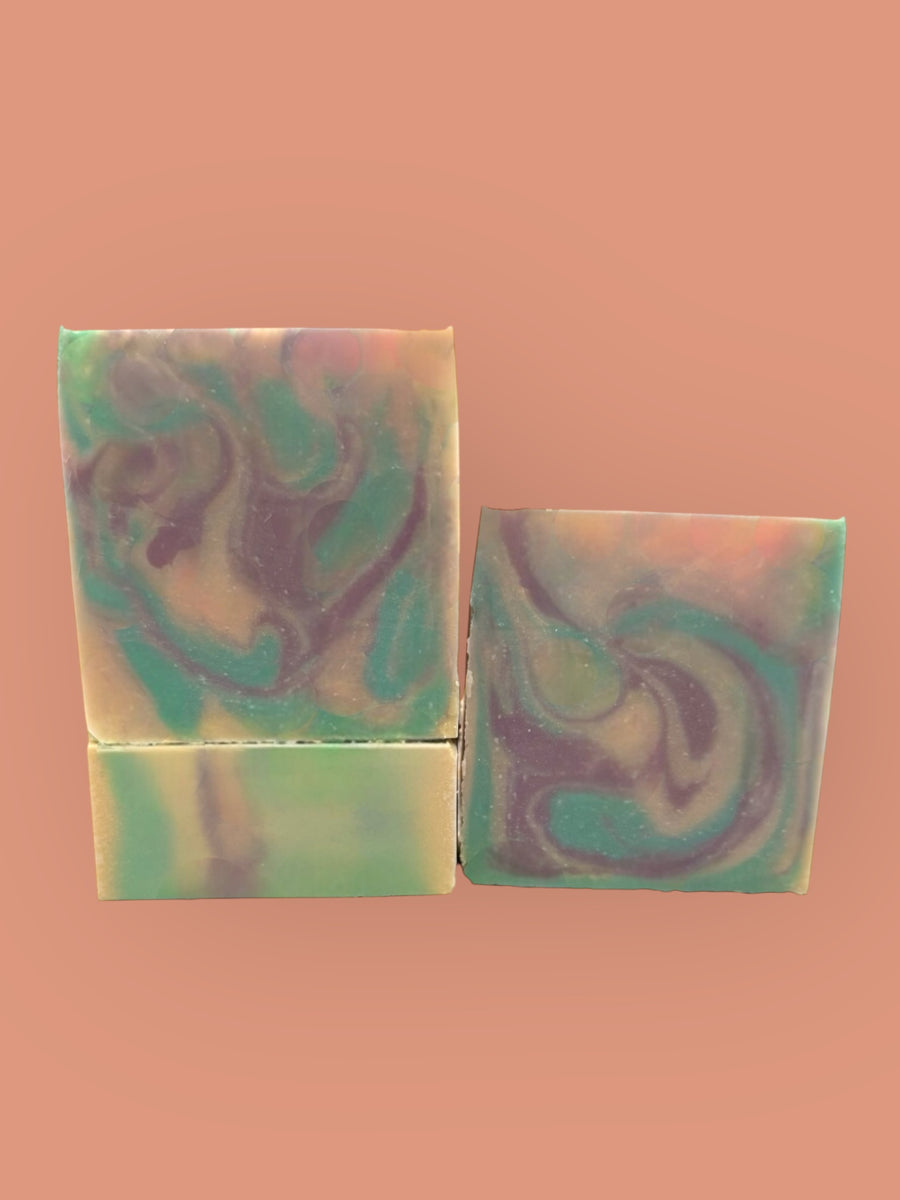 Handmade butterfly pea flower soap bars with green and purple swirls on a peach background