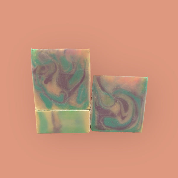 Handmade butterfly pea flower soap bars with green and purple swirls on a peach background
