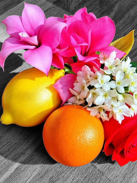 Caesars Palace inspired room spray with bright pink cyclamen, red rose, white blossoms, lemon, and orange on a wooden surface