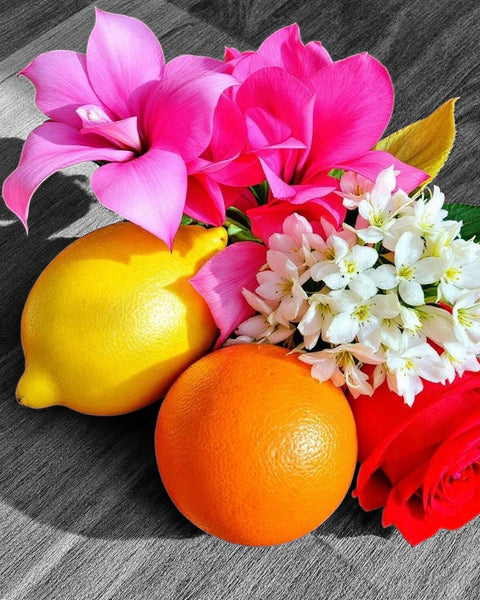 Caesars Palace inspired room spray with bright pink cyclamen, red rose, white blossoms, lemon, and orange on a wooden surface