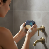 Woman using Glossier You inspired soap bar in a shower, showcasing luxurious lather and fragrance