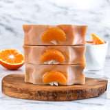 Three bars of Blue Volcano inspired soap Serendipity stacked on wooden board with mandarin slices and orange background