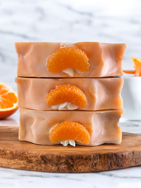 Three bars of Blue Volcano inspired soap Serendipity stacked on wooden board with mandarin slices and orange background