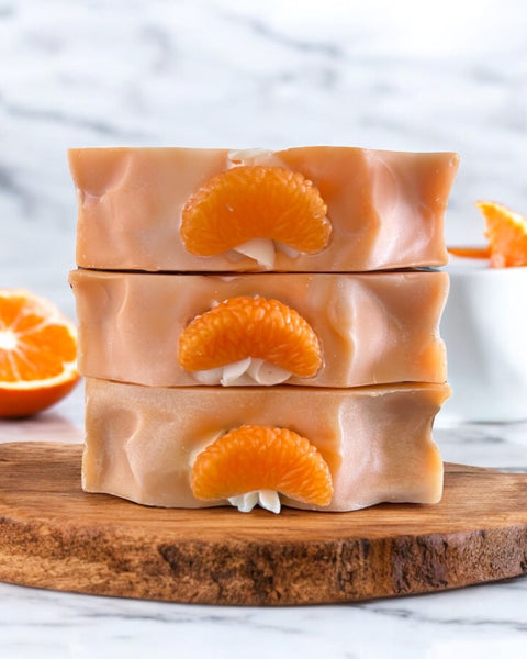 Three bars of Blue Volcano inspired soap Serendipity stacked on wooden board with mandarin slices and orange background