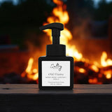 By the Fire inspired luxury foaming hand soap Sultry Scents Old Flame black square pump bottle on wood with campfire flames