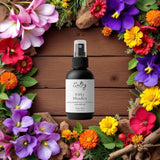 Sultry Scents black body spray bottle on wood backdrop surrounded by colorful flowers Byredo Inspired Bal D'Afrique Body Spray