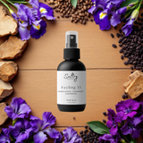 Sultry Scents Santal 33 inspired body spray Feeling 33 black spray bottle on wood surrounded by purple irises sandalwood and beans