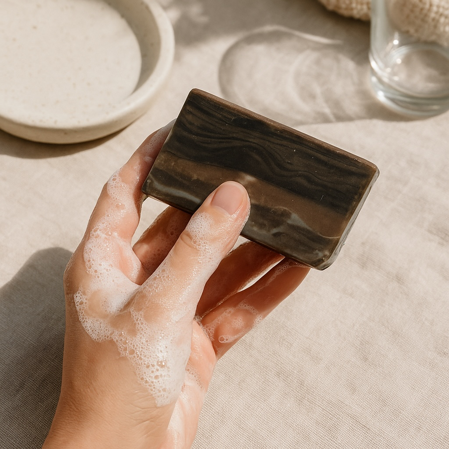 Hand holding a wood fragrance soap that looks like wood with a lather on fingers, on a linen surface