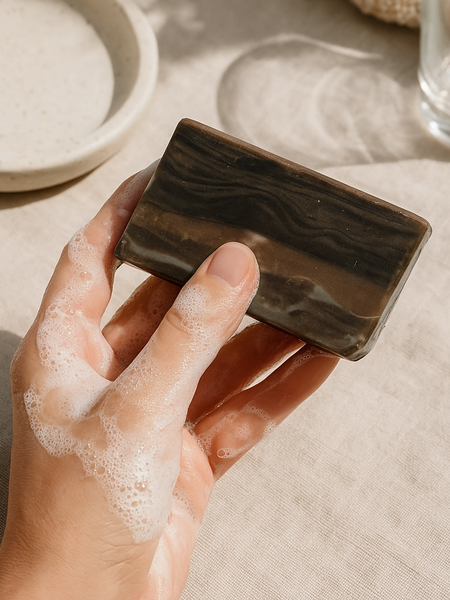 Hand holding a wood fragrance soap that looks like wood with a lather on fingers, on a linen surface